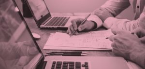 image of hands writing on paper next to a laptop