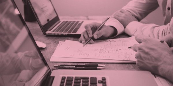 image of hands writing on paper next to a laptop