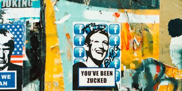 A collage of street art posters on a colourful, weathered wall. The central poster features a stylized black-and-white image of a a smiling Mark Zuckerberg, over a background of Facebook logos, with the text 'YOU'VE BEEN ZUCKED' below. The poster is defaced with graffiti. The surrounding area is filled with layers of torn posters, paint, and scribbles.