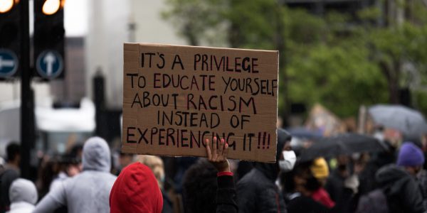 person holding a sign that reads "it's a privilege to educate yourself about racism instead of experiencing it!!!"